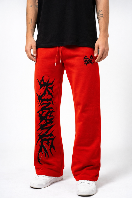 Man wearing Red stacked sweatpants with black tribal lettering reading “KINSANE” on the left side leg and a black logo on the right side