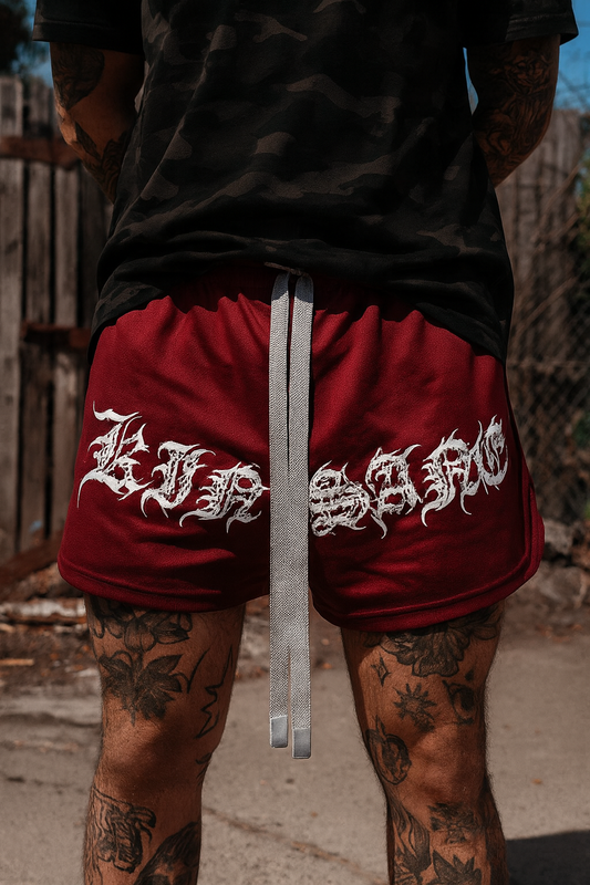 Man wearing Dark red athletic shorts with elastic waistband and gray drawstrings with white tribal lettering reading “KINSANE” across the front