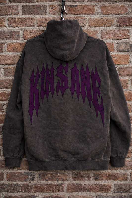 Back view of a vintage gray hoodie with dark purple text reading “KINSANE” Hanging in front of a brick wall