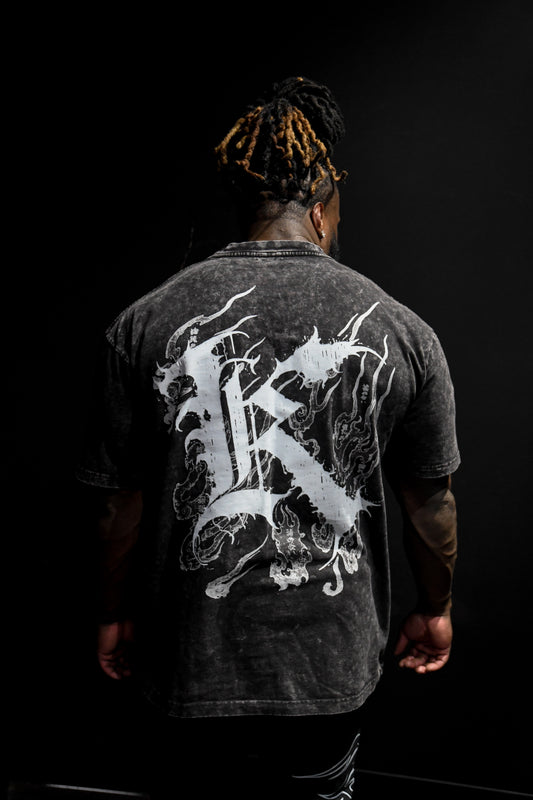 Back view of a man wearing a acid washed black T-shirt with a white logo displaying white Japanese style flames and a white letter “K” and various Japanese text