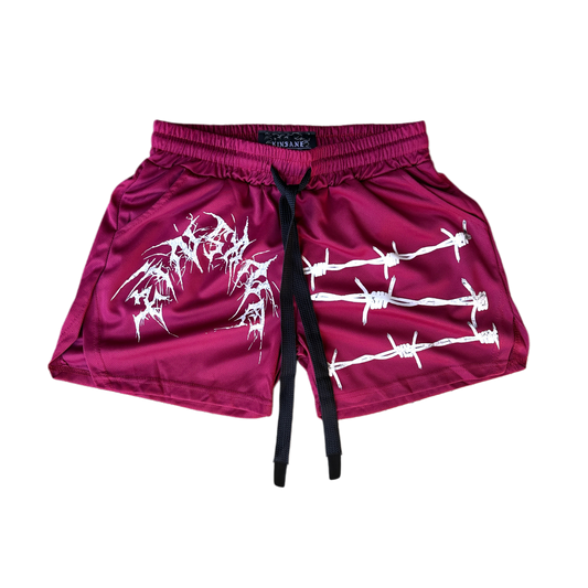 Dark red athletic shorts with elastic waistband and black drawstrings and white tribal lettering reading “KINSANE” on the right leg and white barbed wire design on the left leg