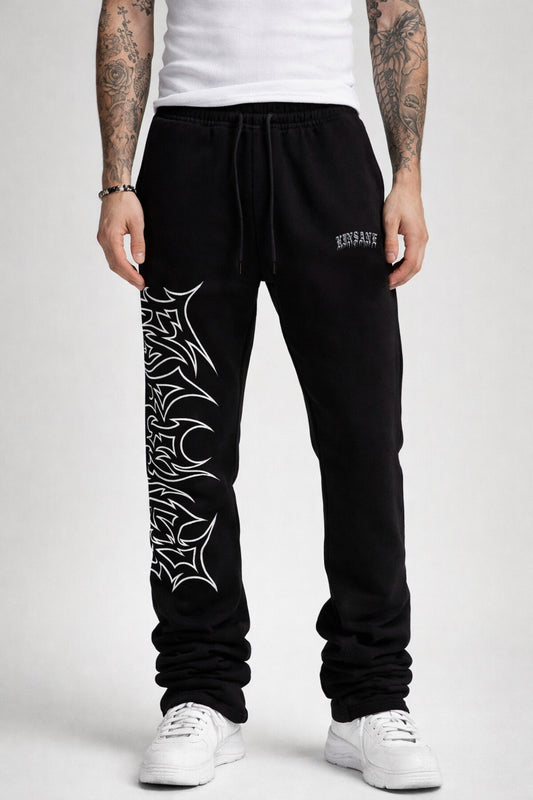 Guy wearing black stacked sweatpants with white outlined tribal lettering reading “forever” on the left side and white old English style lettering reading “KINSANE” on the right side
