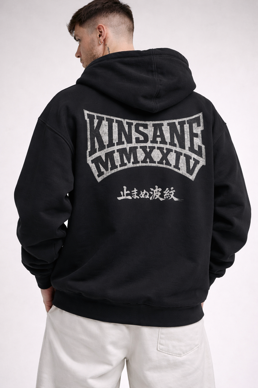 Back view of man wearing a black hoodie with black lettering reading “KINSANE MMXXIV” and white outlining and also white Japanese text