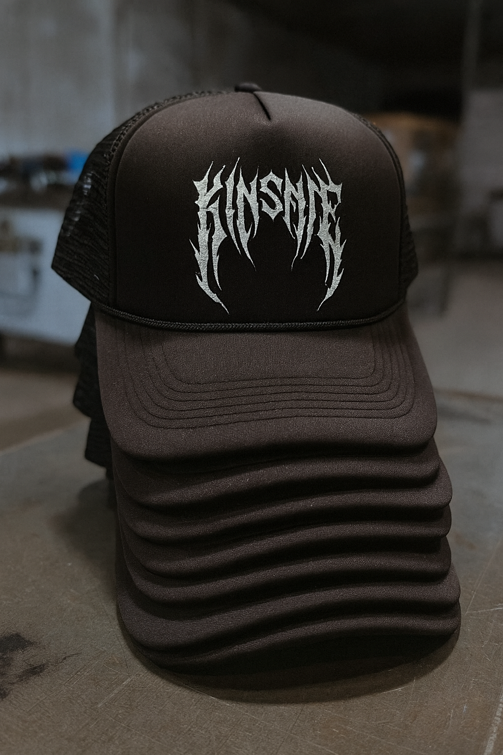 stack of black trucker hats with white tribal lettering reading "KINSANE"