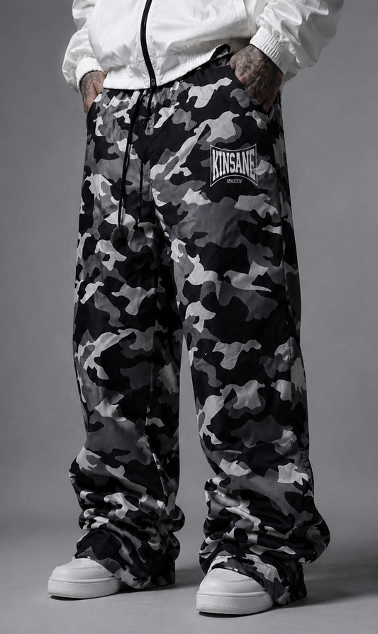 Man wearing Camo baggy sweatpants with white logo lettering on the right side reading “KINSANE MMXXIV” 