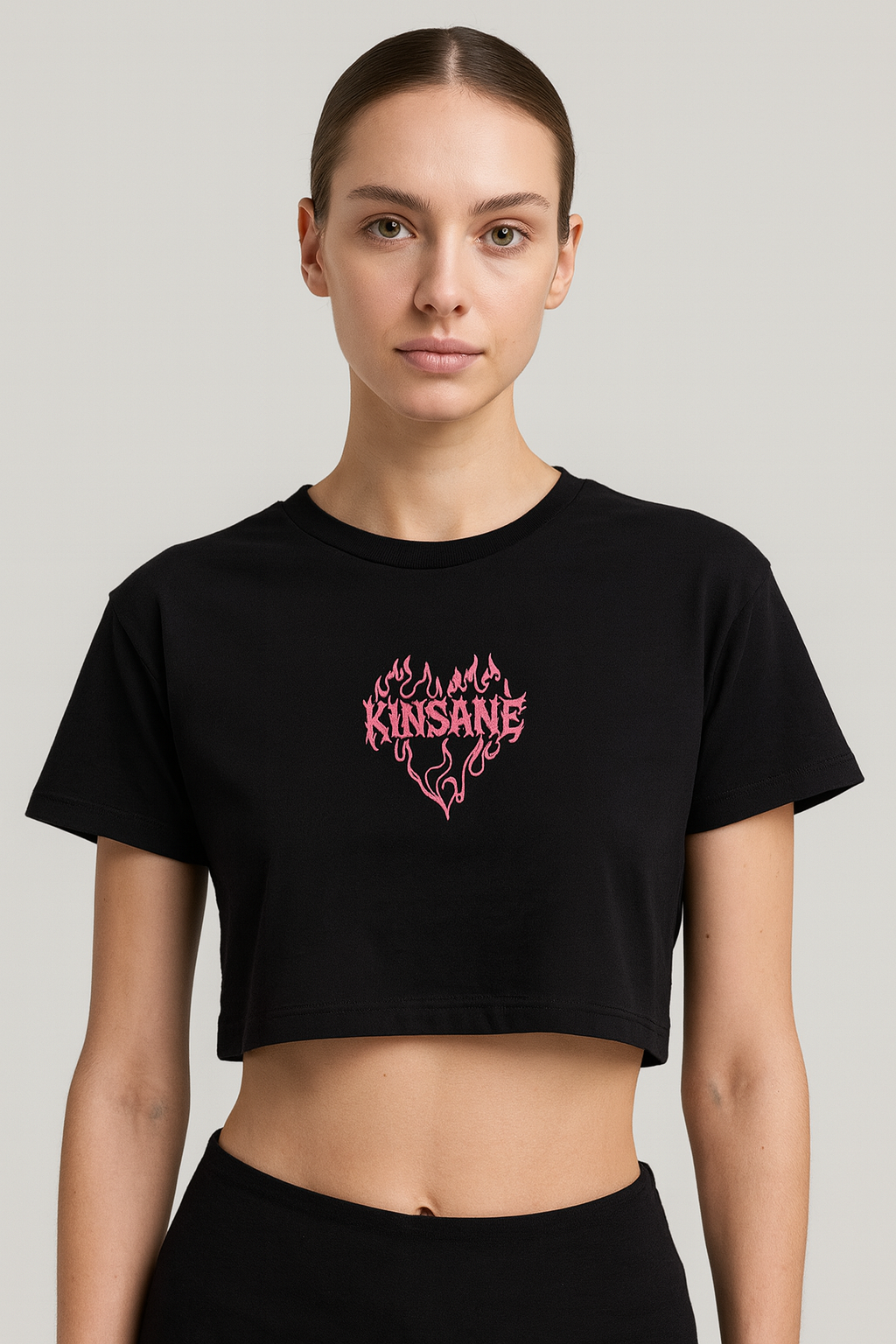 Girl wearing a black crop top T-shirt with pink lettering reading “KINSANE” surrounded by pink flames in the shape of a heart 