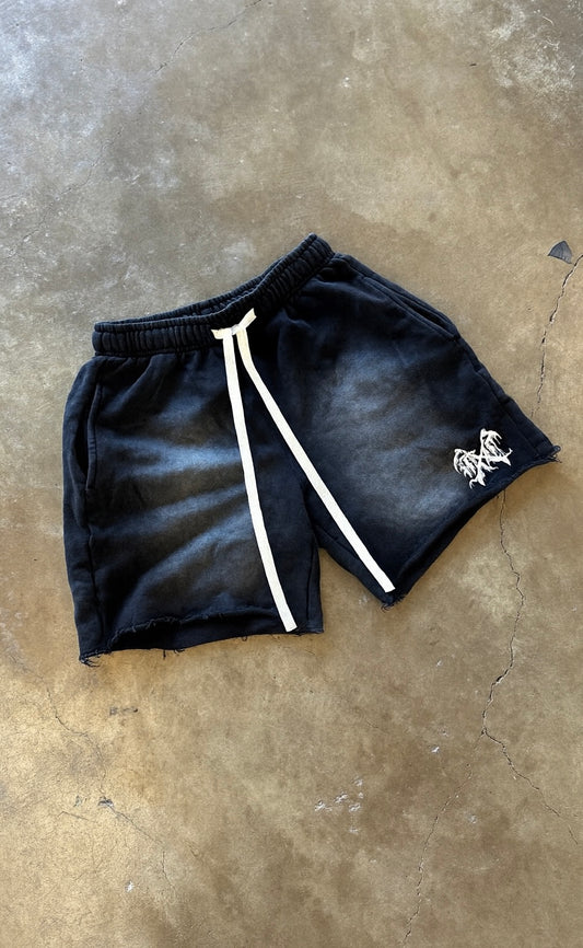 Concrete flat lay of Black acid washed shorts with white drawstrings and white logo on the left leg 