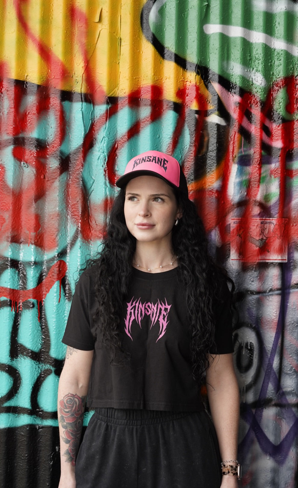 Girl wearing Mesh trucker hat with pink front panel and grey heavy metal lettering reading “KINSANE” 