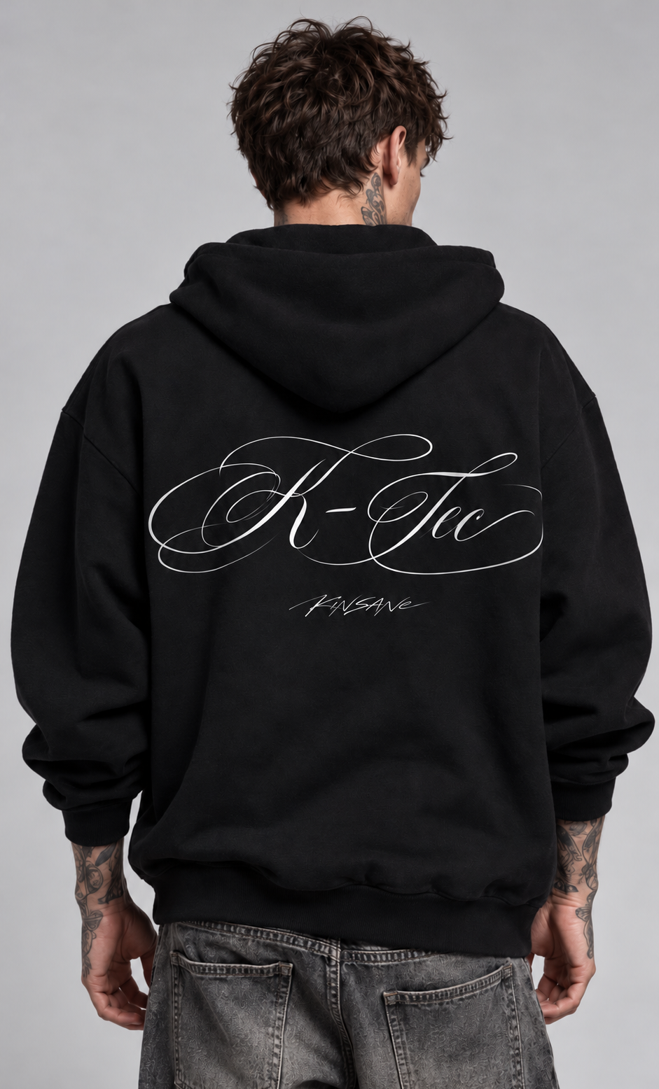 Back view of a man wearing a black hoodie with white cursive text reading “K-Tec” and “Kinsane” 