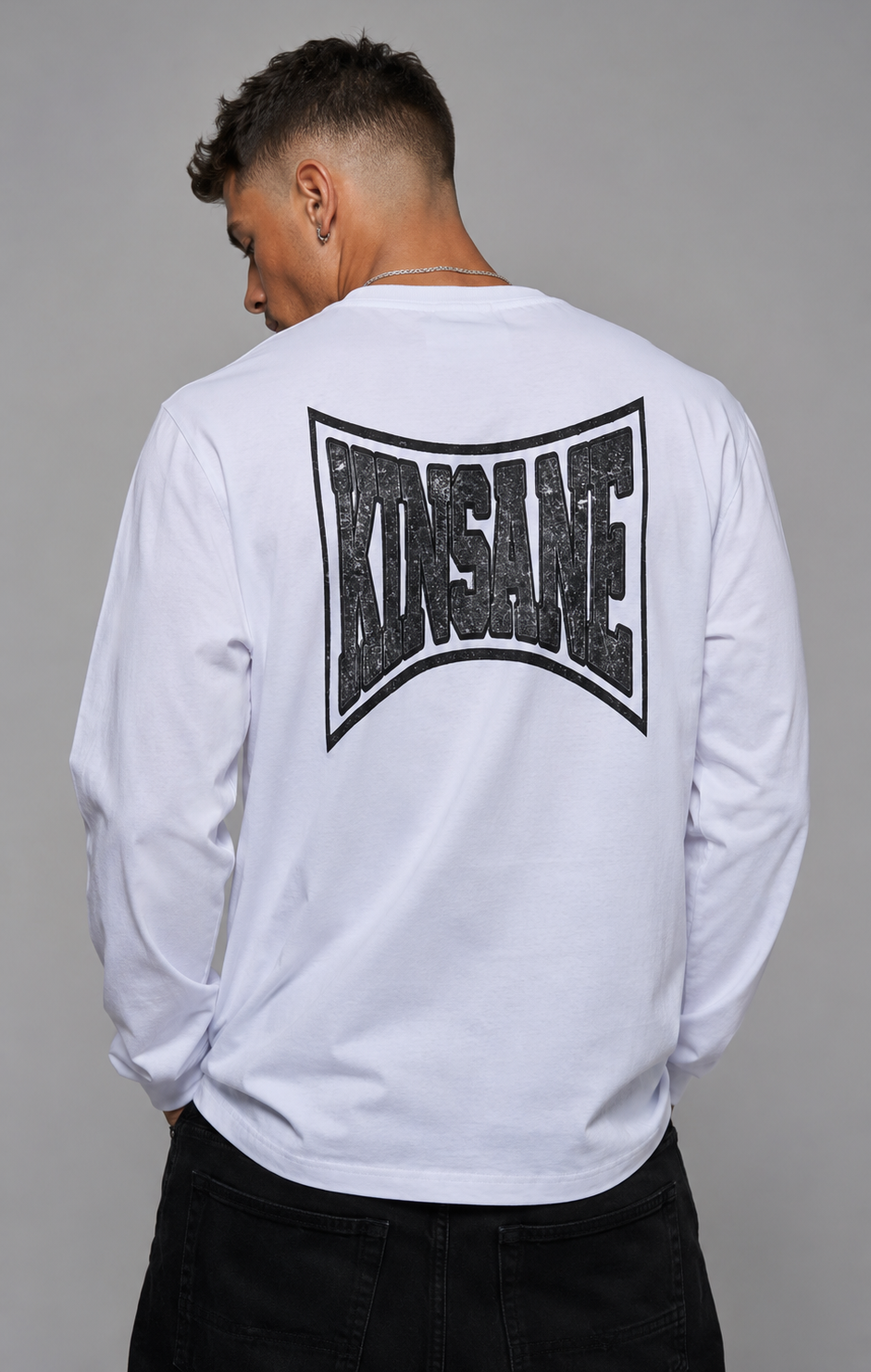 Back view of a man wearing a white long sleeve shirt with black logo and text reading “KINSANE” 