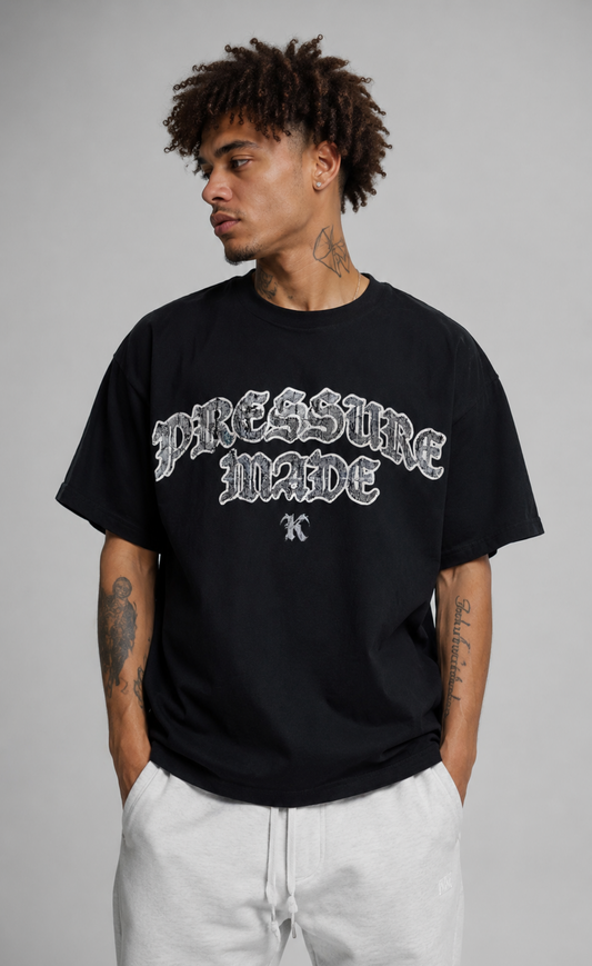 Man wearing black t shirt with white distressed text reading “PRESSURE MADE K” 