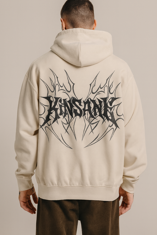 Back view of a man wearing a beige hoodie with black tribal designs and black lettering reading “KINSANE” 