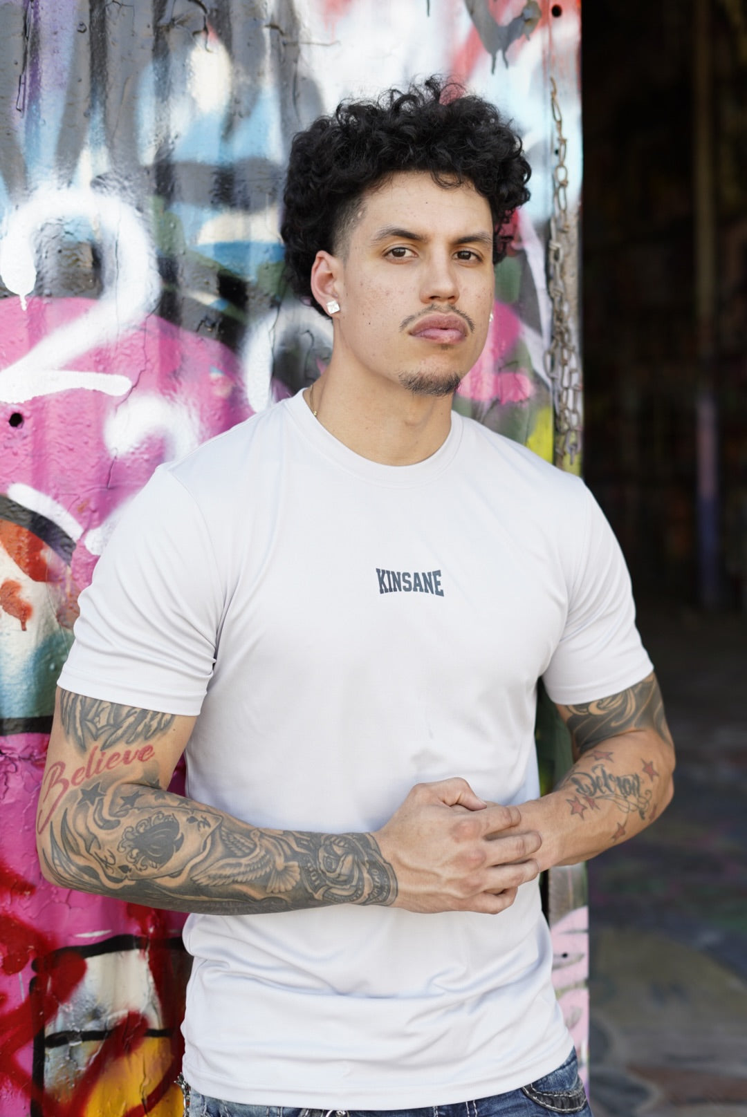 Man wearing Gray dry fit t shirttail with dark blue lettering reading “KINSANE” 