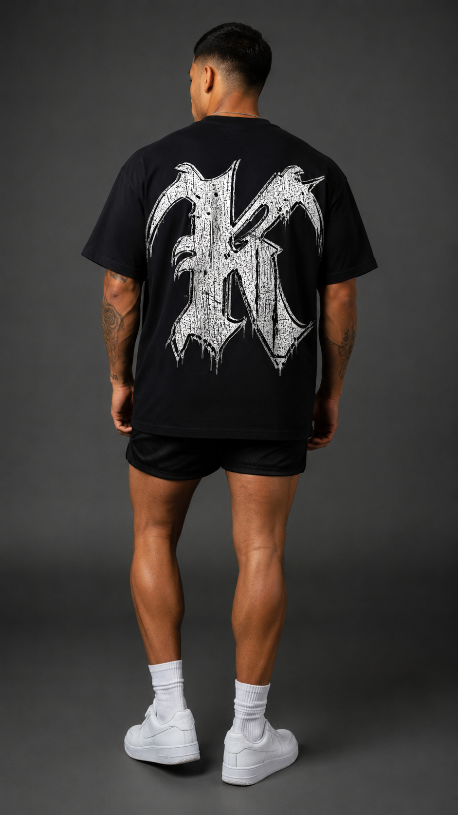 Back view of a man wearing a black t shirt with a white and black logo of the letter “K”