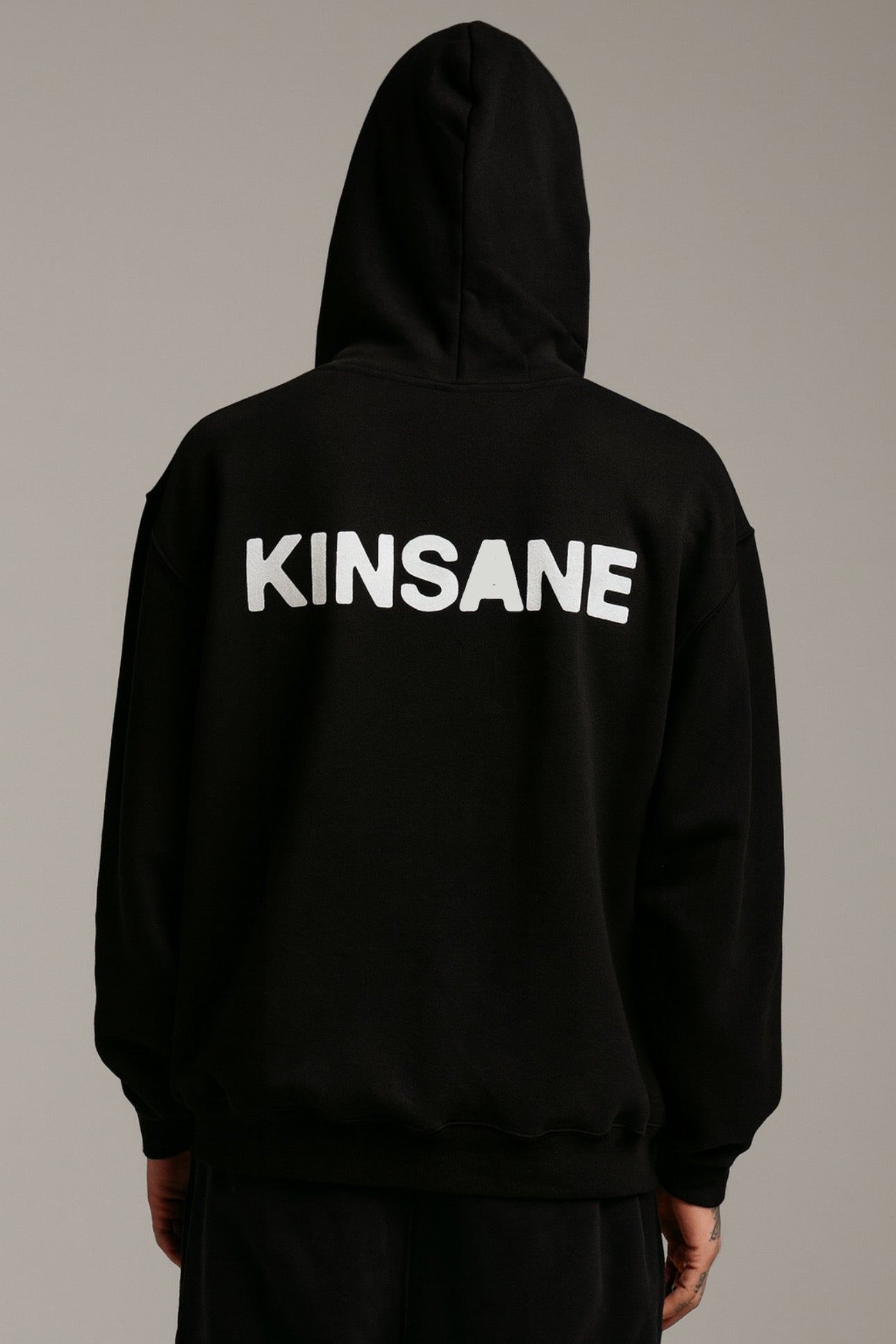 Back view of a man wearing a black hoodie with white text reading “KINSANE” 