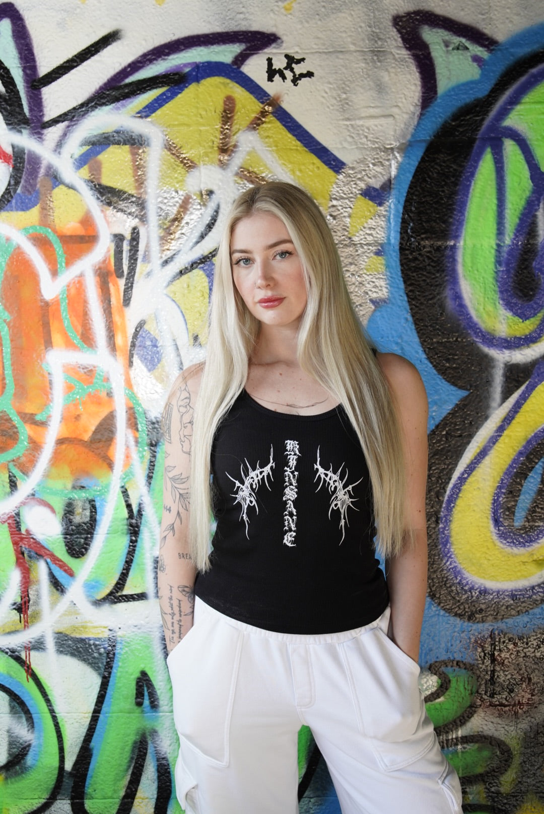 Girl wearing Black tank top with white old English style lettering reading “KINSANE” and white tribal designs 
