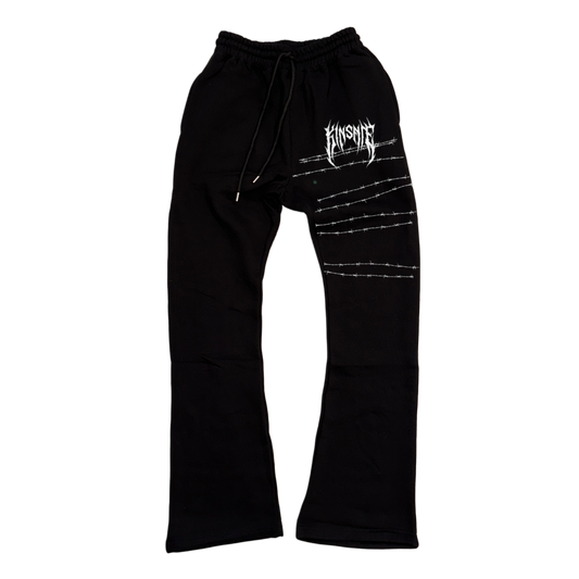 Black stacked sweatpants with white tribal lettering reading “KINSANE” on the right side with white barbed wire behind it 