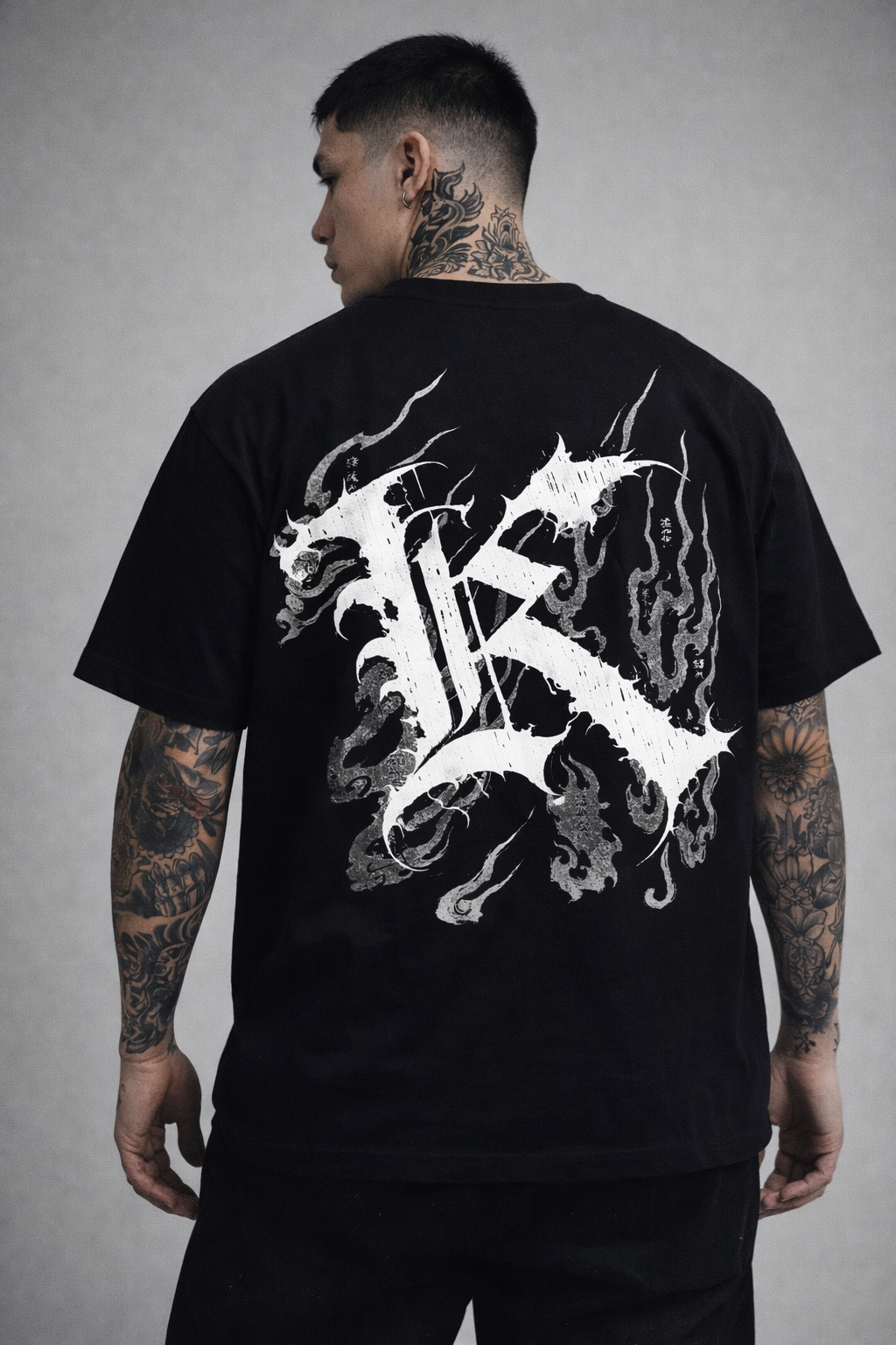 Back view of a man wearing a black T-shirt with a white logo displaying white Japanese style flames and a white letter “K” and various Japanese text 