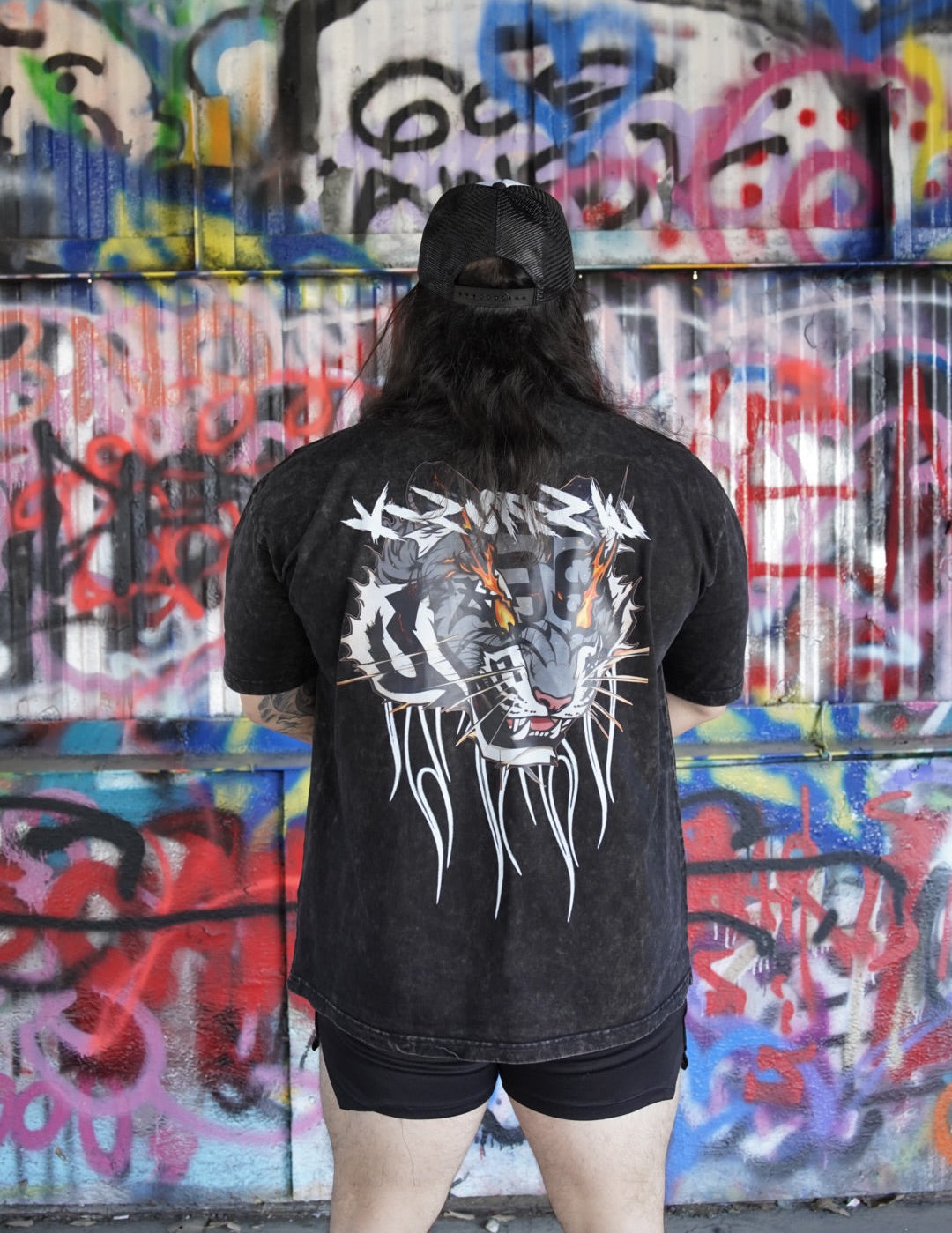 Back view of a man wearing a black acid washed t-shirt with a tiger on fire design and white lettering reading “KINSANE” 