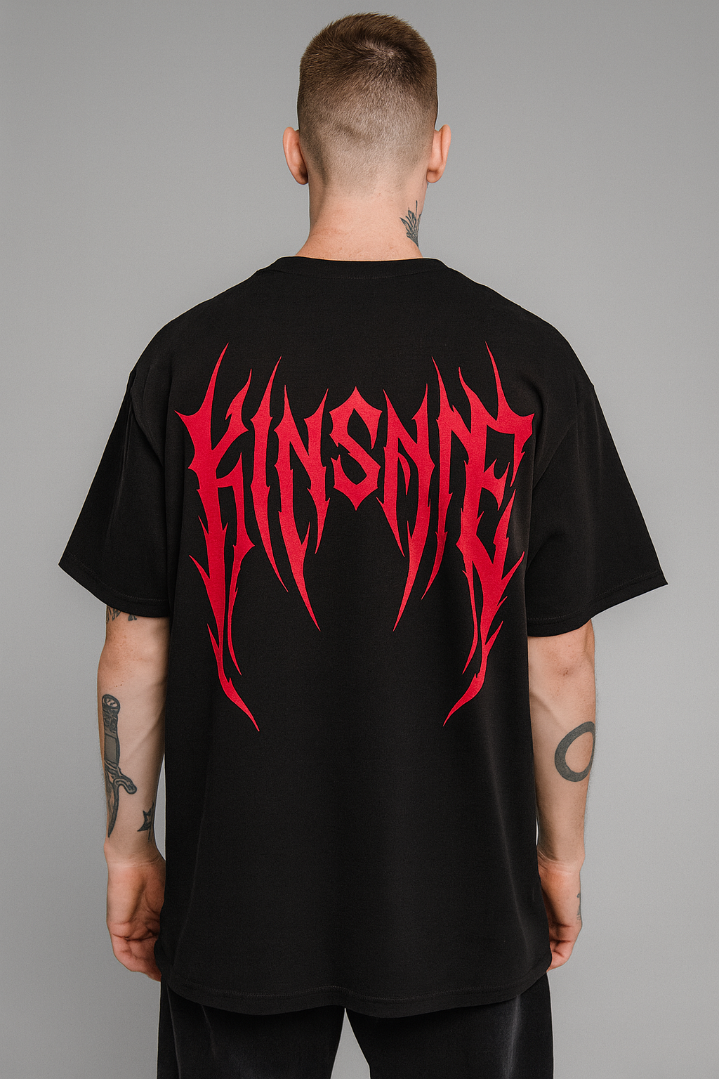 Back view of a man wearing a black T-shirt with red tribal lettering reading “KINSANE” 