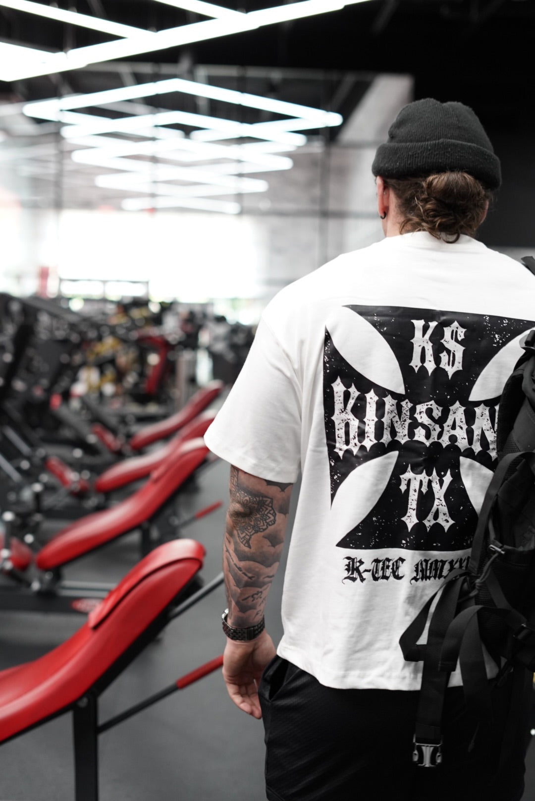 Back view of a man wearing a white t shirt with black logo and white text reading “KS KINSANE TX” and black text reading “K-TEC MMXXIV” 