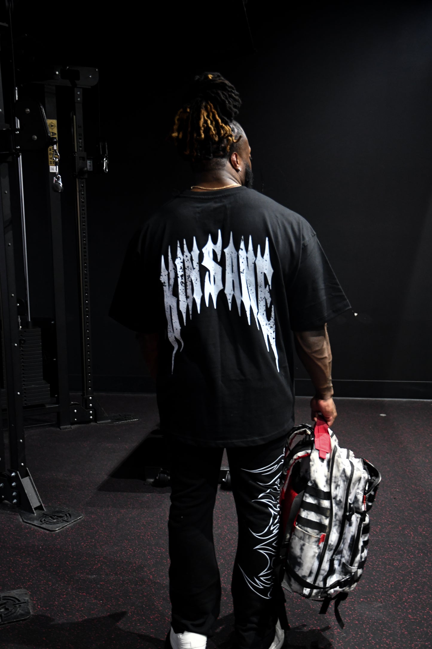 Back view of a man wearing a black t-shirt with white distressed text reading “KINSANE” 