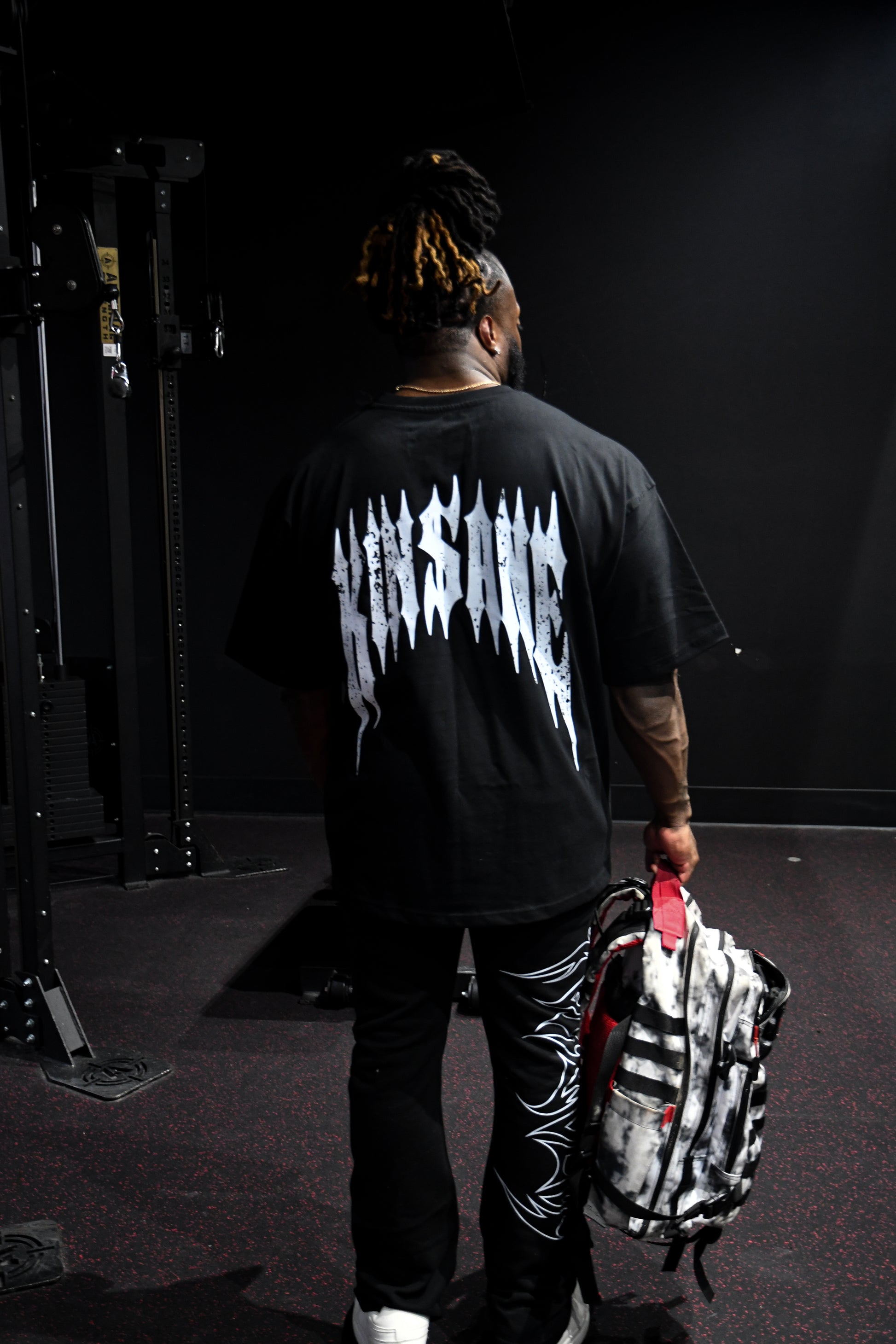 Back view of a man wearing a black t-shirt with white distressed text reading “KINSANE” 