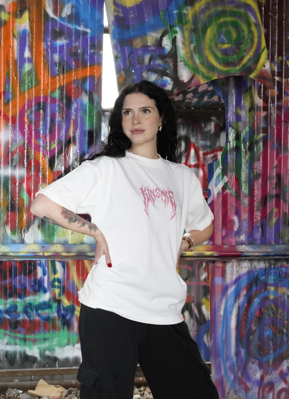 person wearing white t-shirt with pink text on the front reading "KINSANE" 