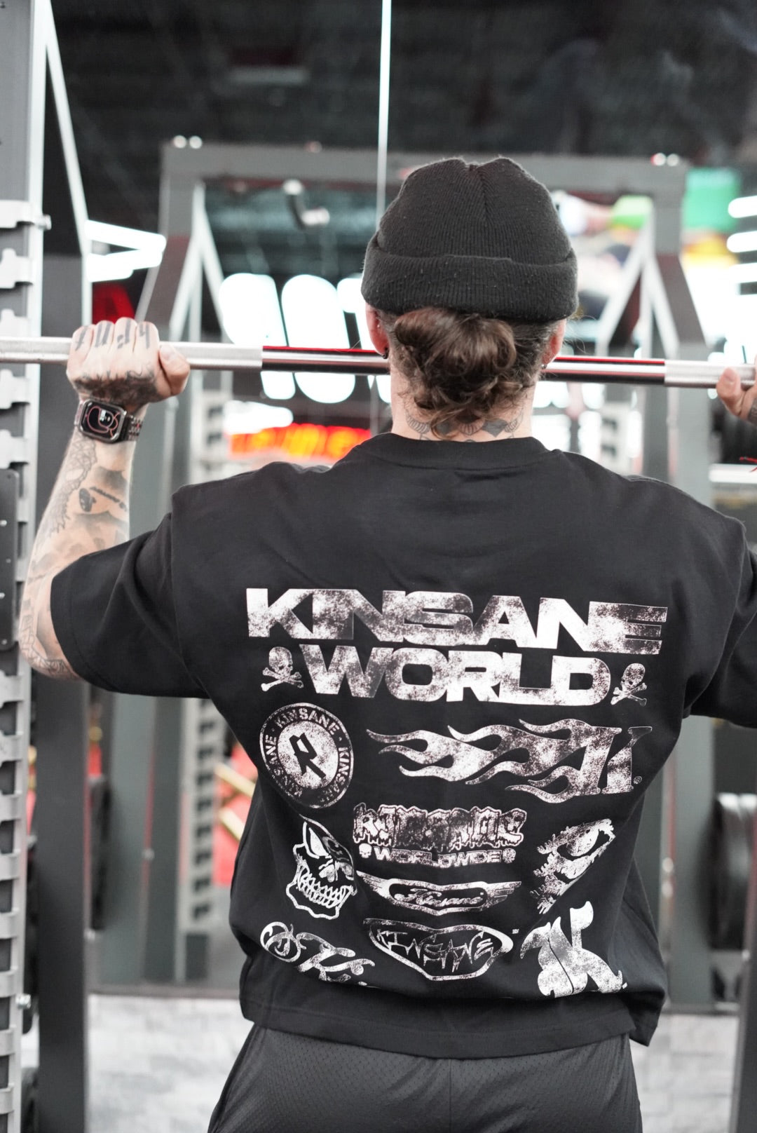 Back view of a man wearing a black t-shirt with multiple white kinsane themed logos reading “KINSANE” stacked on top of each other and white text reading “KINSANE WORLD” 