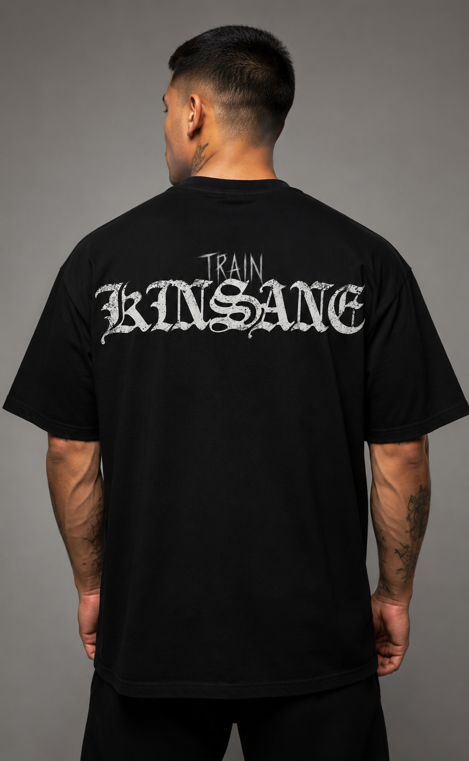 Back view of a man wearing a black t shirt with white text reading “TRAIN KINSANE” 