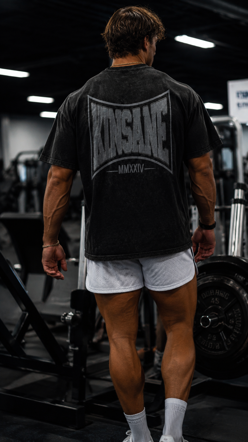 Back view of a man in the gym wearing a acid washed black t shirt with grey logo and text reading “KINSANE MMXXIV” 