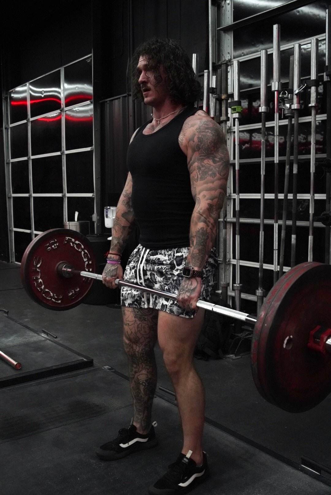 Side view of a Man lifting weights wearing white and black snakeskin pattern athletic shorts with white drawstrings 