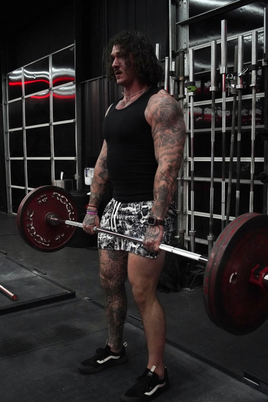 Side view of a Man lifting weights wearing white and black snakeskin pattern athletic shorts with white drawstrings 