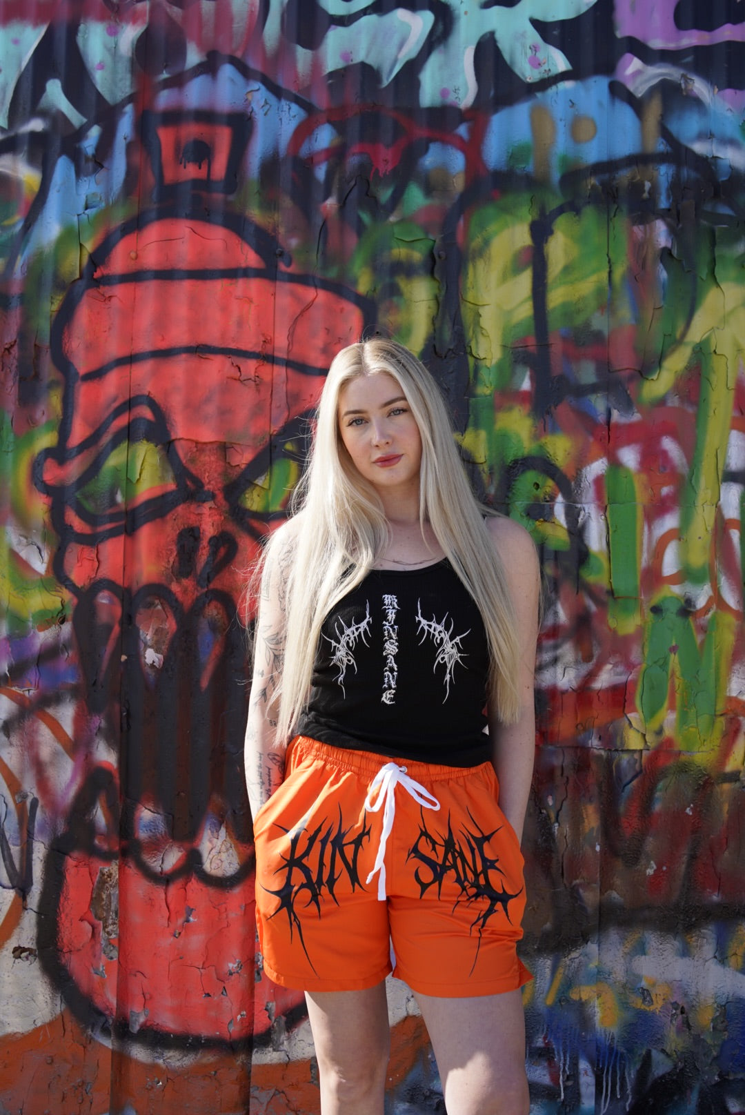 Girl wearing Orange trunks with white drawstrings and black tribal lettering across the middle reading “KINSANE” 