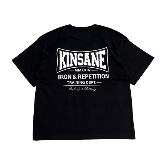 Back view of a black t shirt with white logo and white text reading “KINSANE MMXXIV IRON & REPETITION TRAINING DEPT. BUILT BY ADVERSITY” 