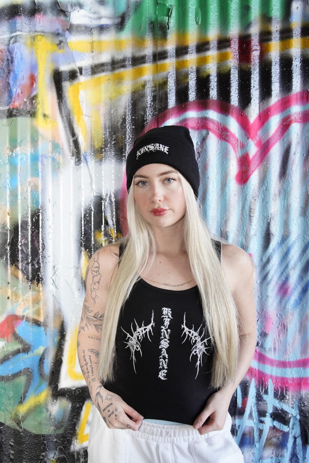 Girl wearing Black beanie with silver old English style lettering reading “KINSANE” 