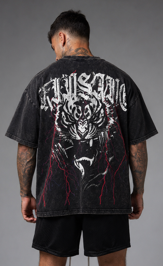 Back view of a man wearing a black acid washed t-shirt with a tiger in flames and red lightning holding a dumbbell in its mouth design and white lettering reading “KINSANE”