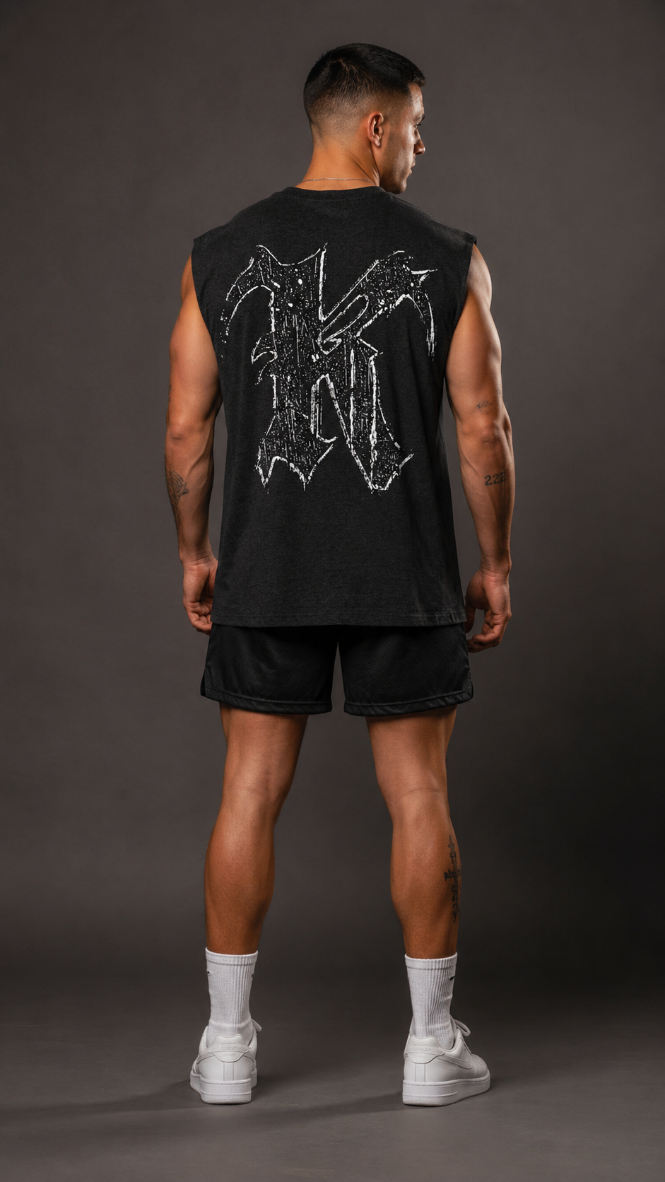 Back view of a man wearing a dark gray sleeveless shirt with white logo in the letter “K” 