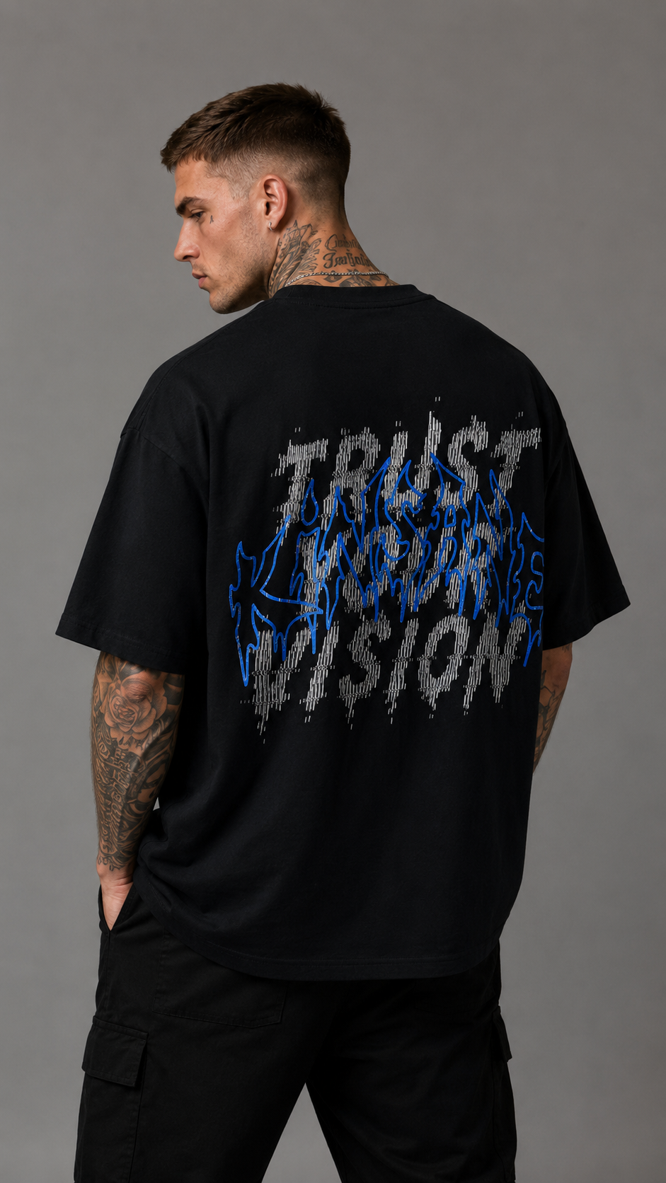Back view of a man wearing a black t shirt with white static text reading “TRUST YOUR VISION” and blue outlined text reading “KINSANE” 