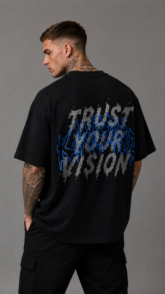 Back view of a man wearing a black t shirt with white static text reading “TRUST YOUR VISION” and blue outlined text reading “KINSANE” 