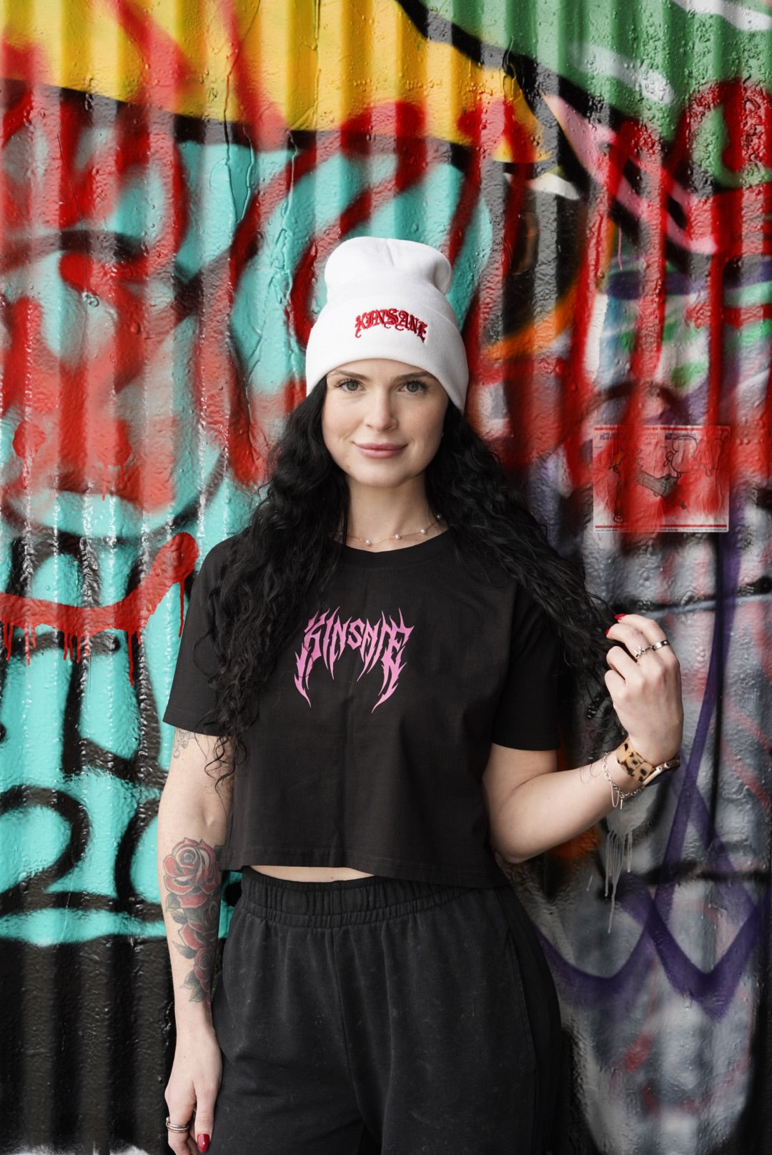 Girl wearing White beanie with red old English style lettering reading “KINSANE” 