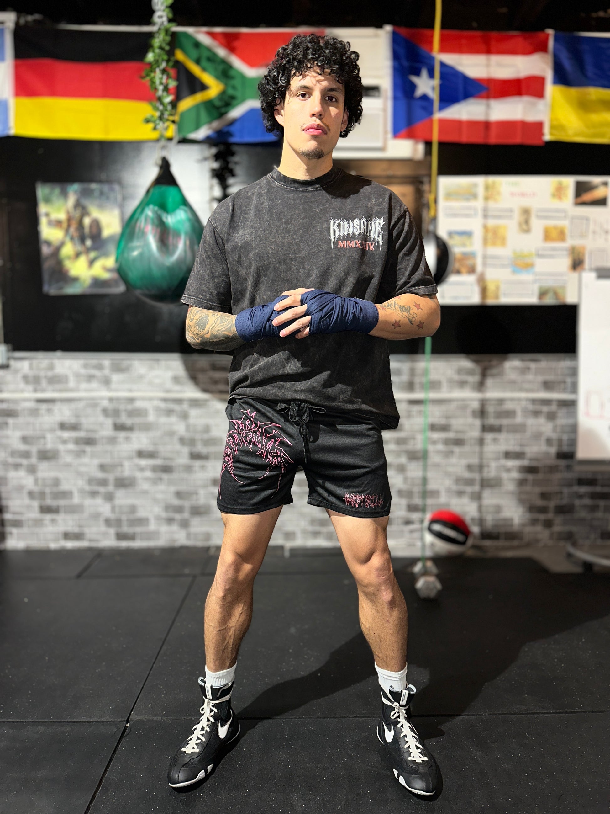 Man wearing Black athletic shorts with elastic waistband and black drawstrings with red outlined tribal lettering reading “KINSANE” on the right leg and red tribal outlined lettering reading “HARDTOKILL” on the left leg