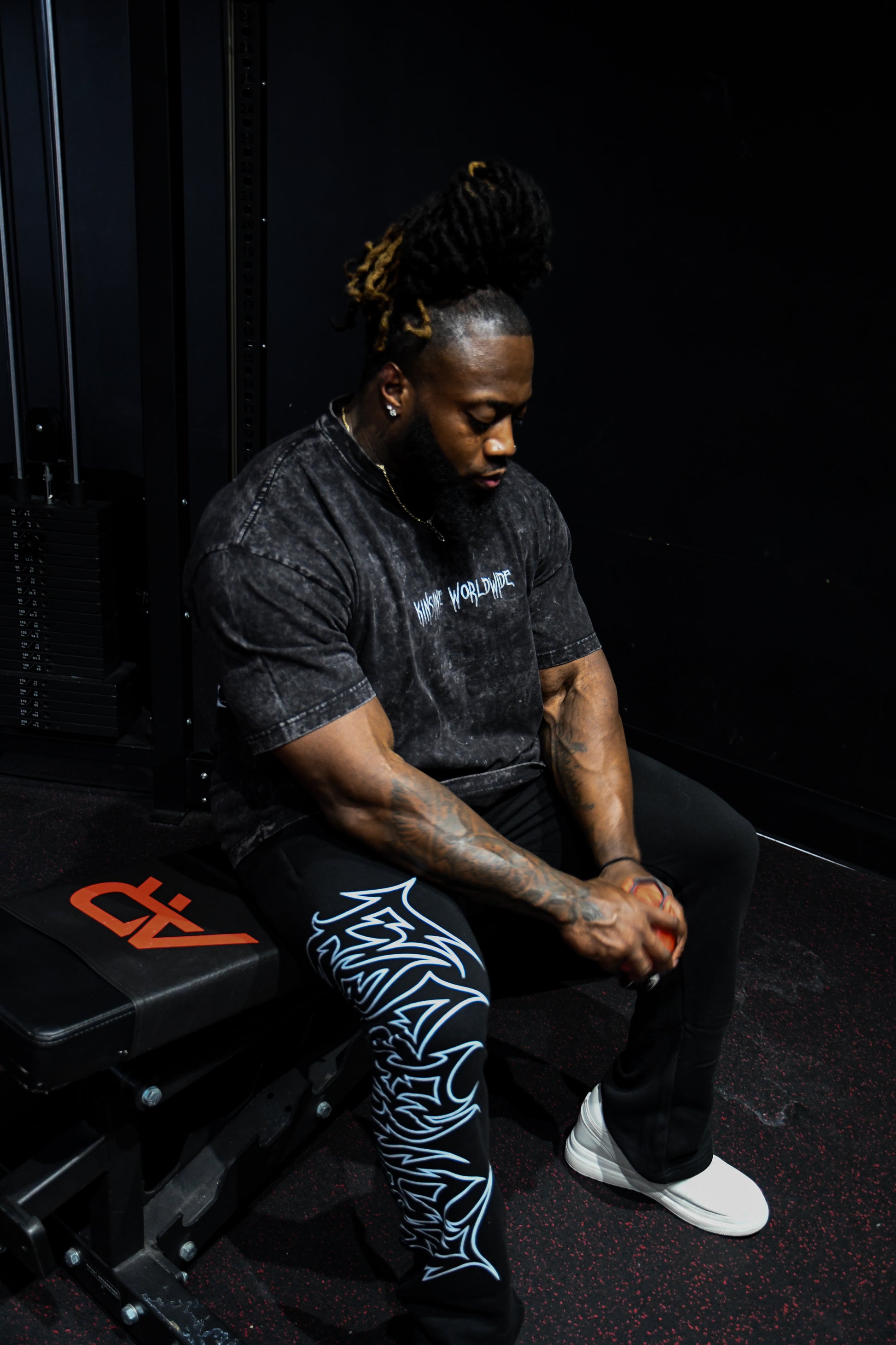 Man sitting down with black acid washed t-shirt with white text on the front reading “KINSANE WORLDWIDE” 