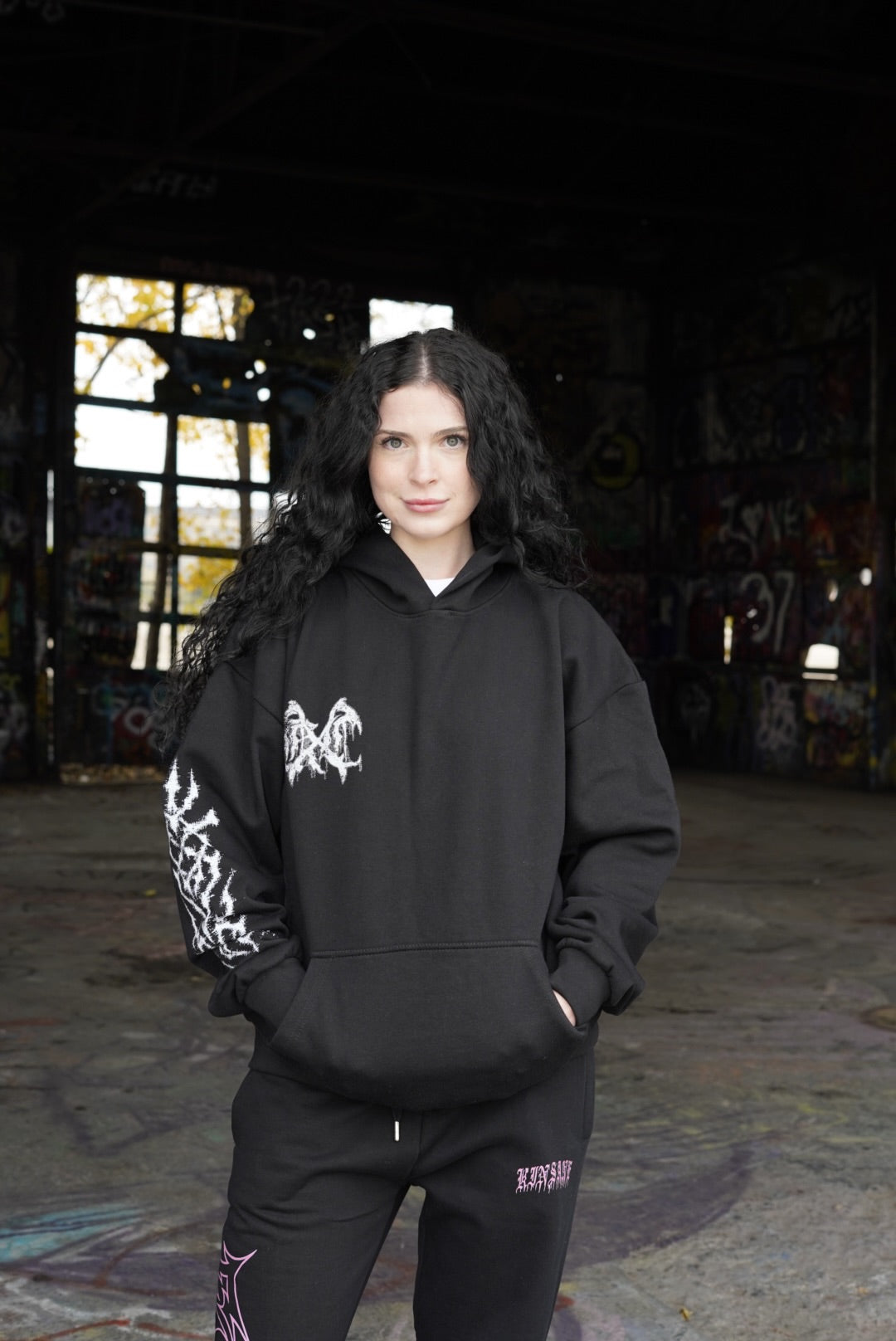 Girl wearing a black hoodie with a white logo and white tribal design on the sleeve on the left side 