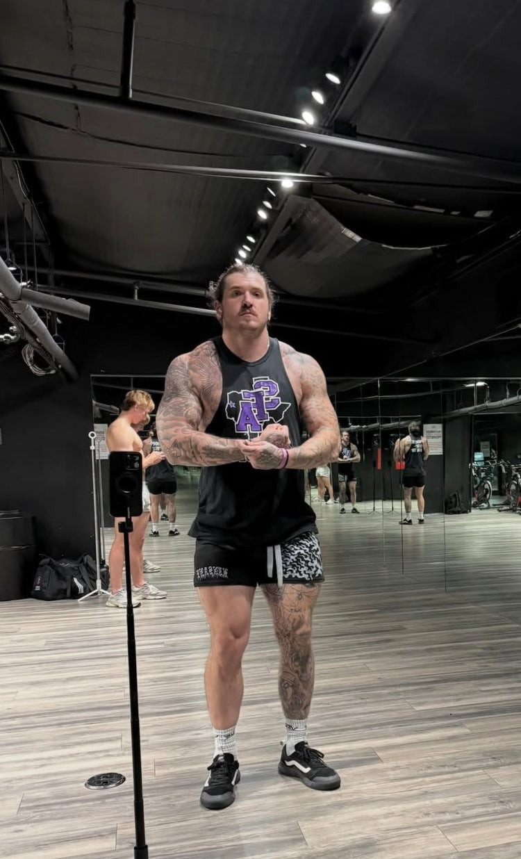 Man in a gym wearing black athletic shorts with gray strings and blue and gray flames on the right side and white text reading “KINSANE” on the left side 