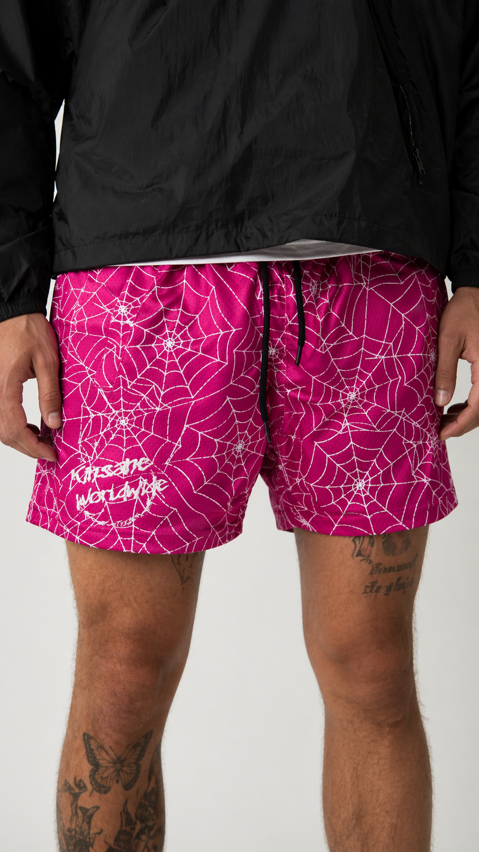 Man wearing Pink athletic shorts with webbed design and white lettering reading “KINSANE WORLDWIDE” and black drawstrings 