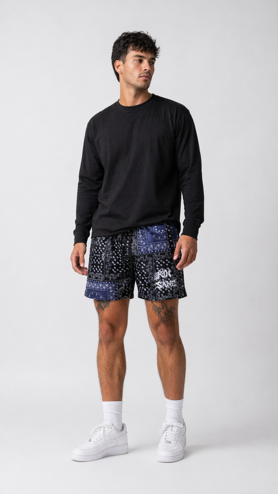 Man wearing Black shorts with white and blue bandana design and black drawstrings and white lettering reading “KINSANE “ on the left leg 