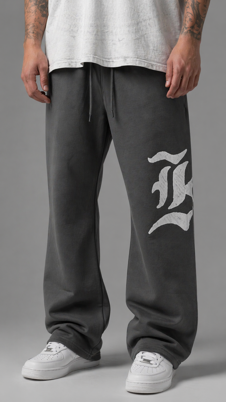 Man wearing Gray stacked sweatpants with gray drawstrings and a white logo of a “K” on the left leg