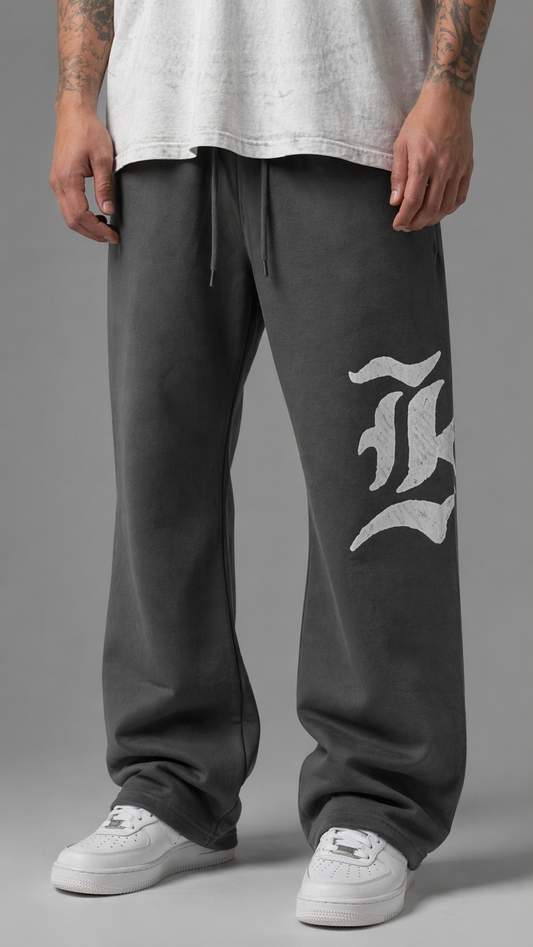 Man wearing Gray stacked sweatpants with gray drawstrings and a white logo of a “K” on the left leg
