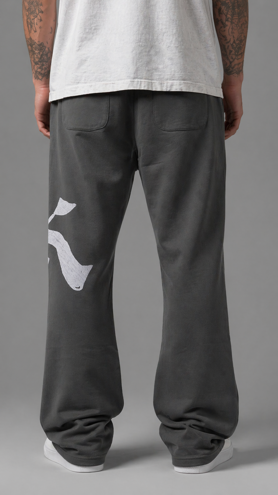 Back view of man wearing Gray stacked sweatpants with gray drawstrings and a white logo of a “K” on the left leg